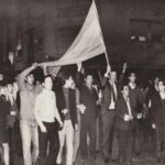 Jóvenes marchando por calle Corrientes con una bandera argentina en alto.